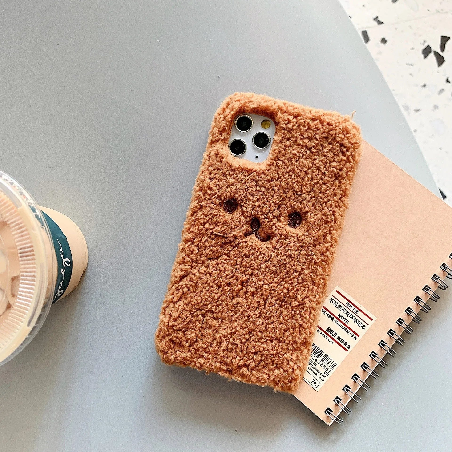 Brown embroidered plush cartoon bear face on a clear TPU iPhone 11 case, showing raised edges.