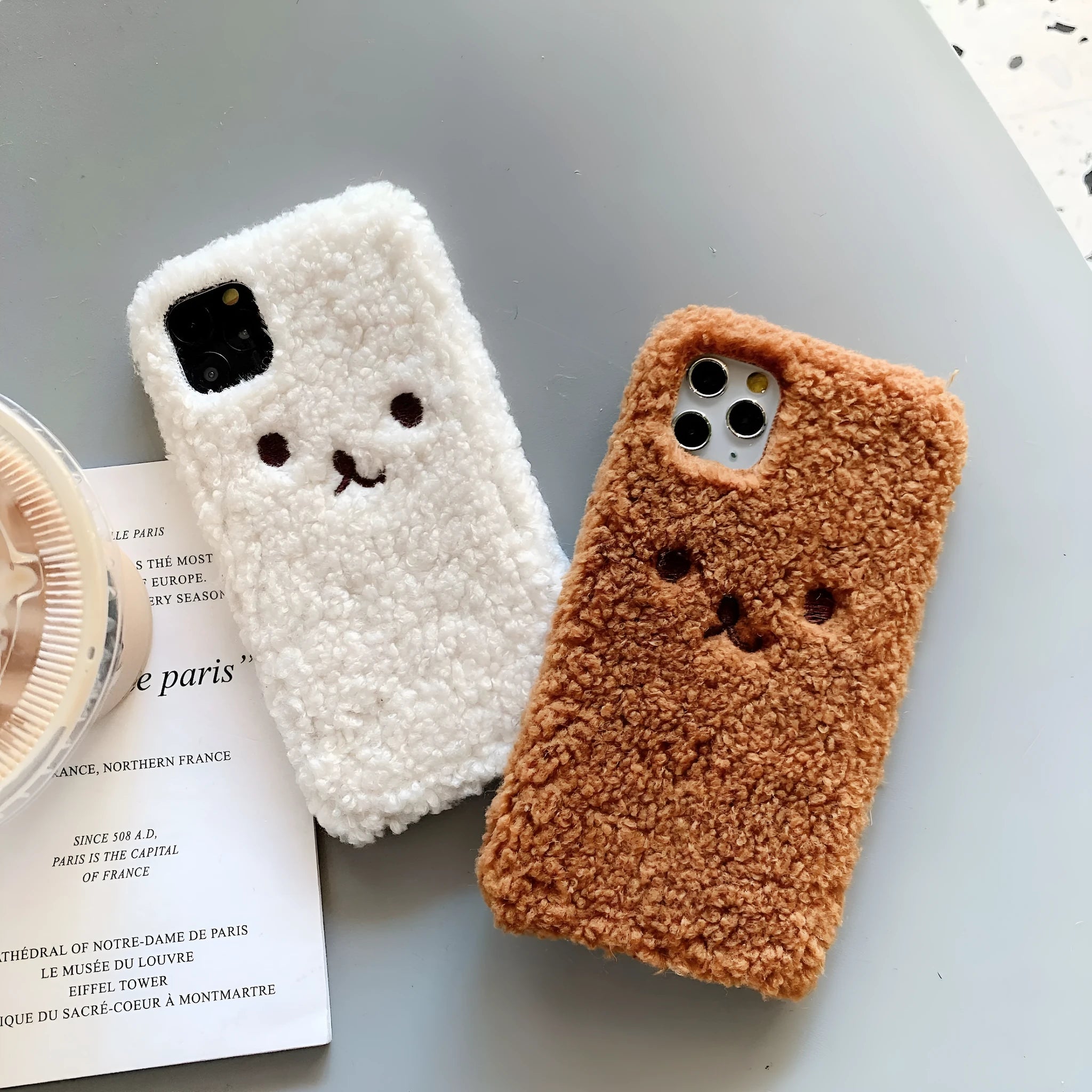 Brown embroidered plush cartoon bear face on a clear TPU iPhone 11 case, showing raised edges.