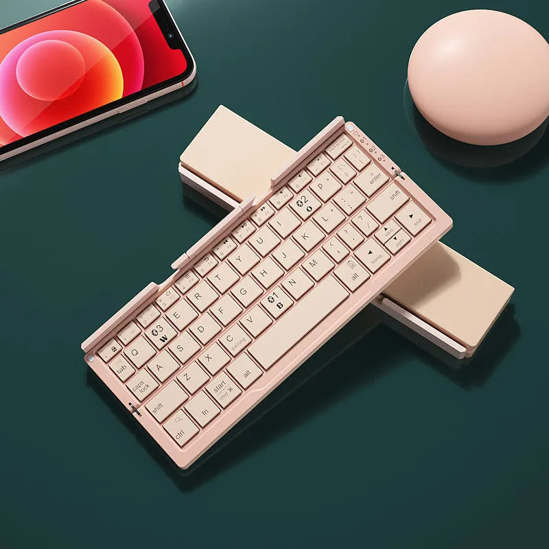 Silver white aluminium folding Bluetooth keyboard shown open next to a smartphone propped on its hidden stand.