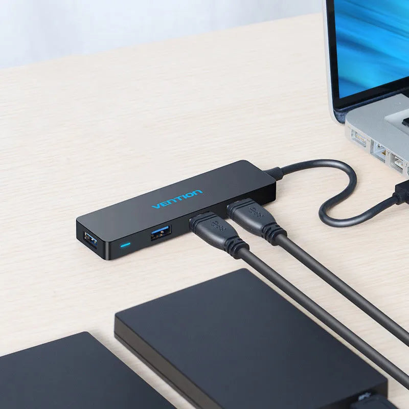 Black four-port USB 3.0 hub with a short cable, nickel-plated ports, and ABS plastic body on a desk