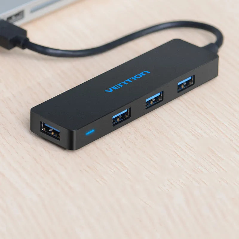 Black four-port USB 3.0 hub with a short cable, nickel-plated ports, and ABS plastic body on a desk