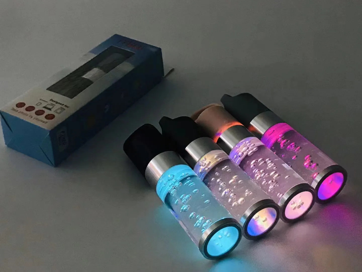 Compact colourful Bluetooth speaker with glowing crystal lights, shown in pink, black, silver grey, and green colour options.