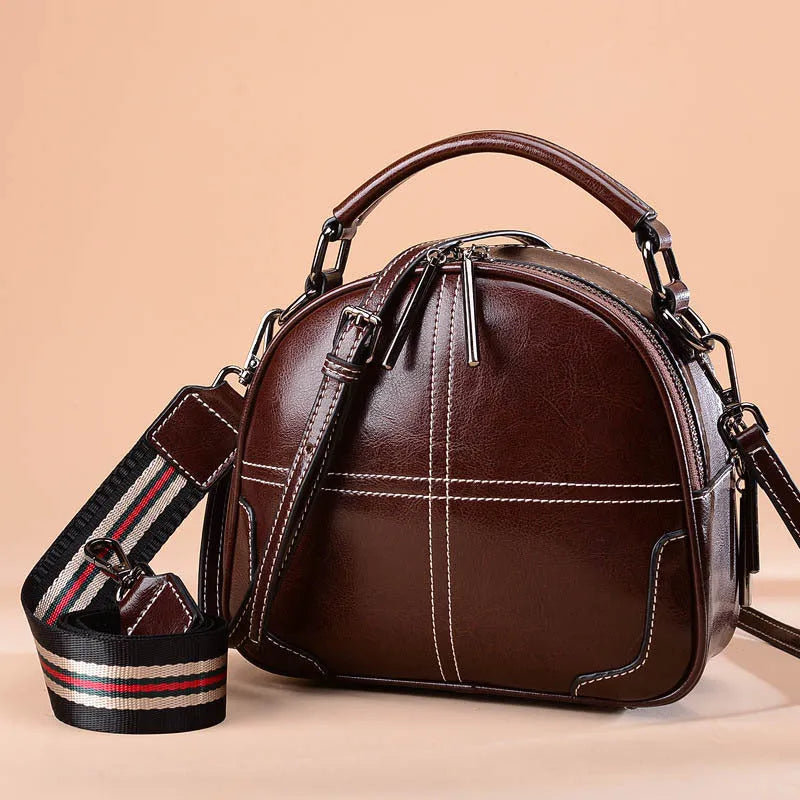 Wine red leather crossbody bag with a structured round shape, shown with its zipper open.