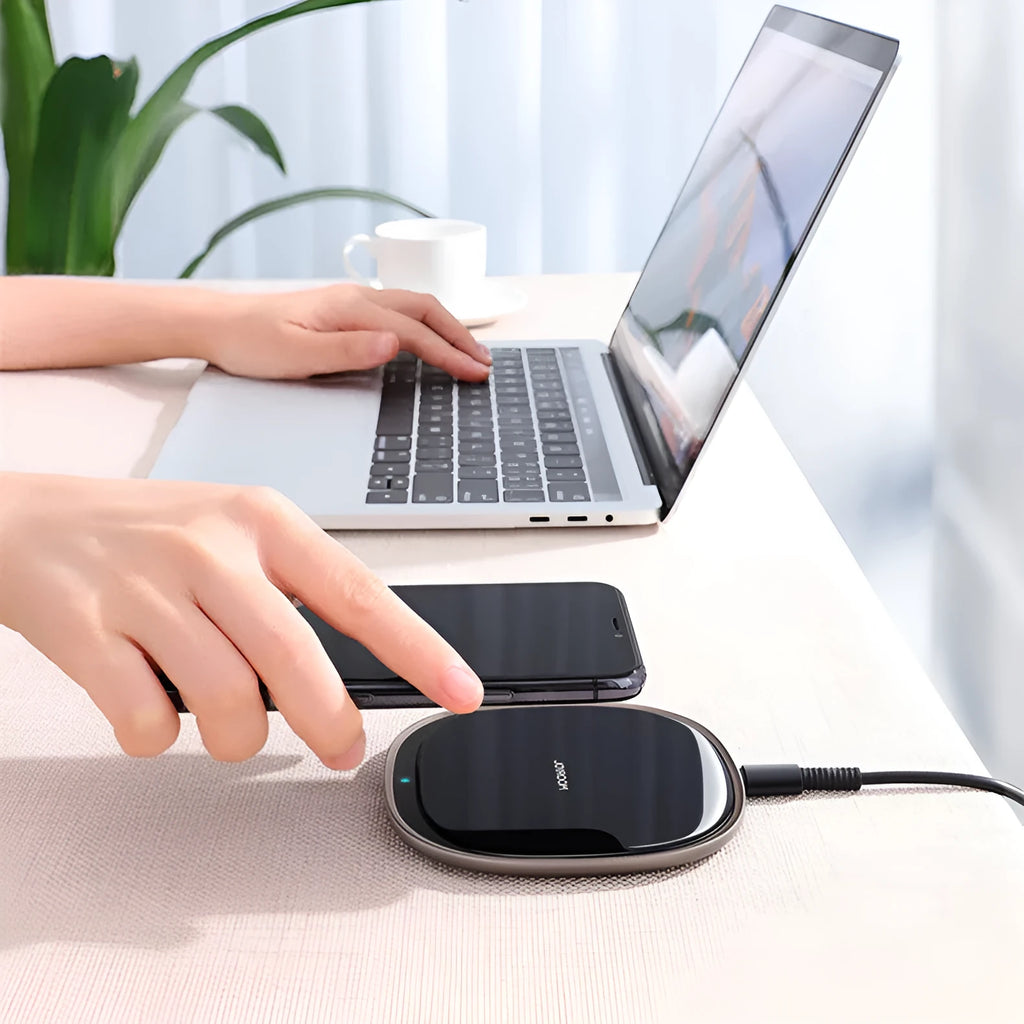 Black square wireless charging pad with glass top and zinc alloy rim on a wooden desk