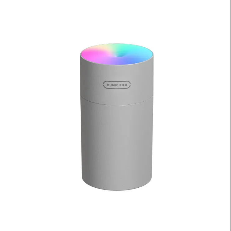 Pink USB mini humidifier with LED lights on wooden desk beside laptop