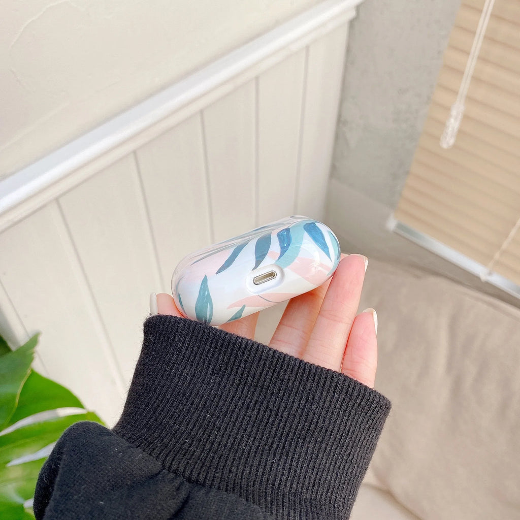 Blue TPU AirPods case with painted tropical banana leaf design, shown next to a green variant.