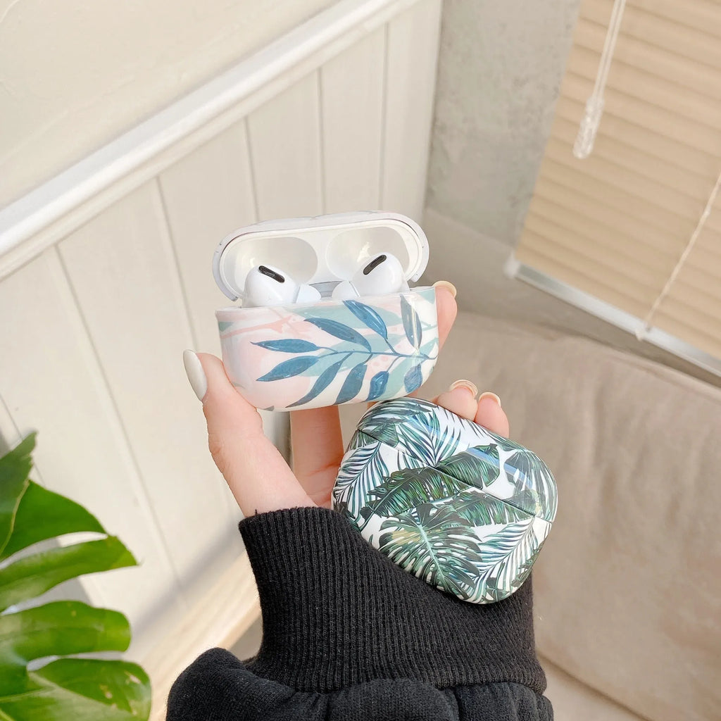 Blue TPU AirPods case with painted tropical banana leaf design, shown next to a green variant.