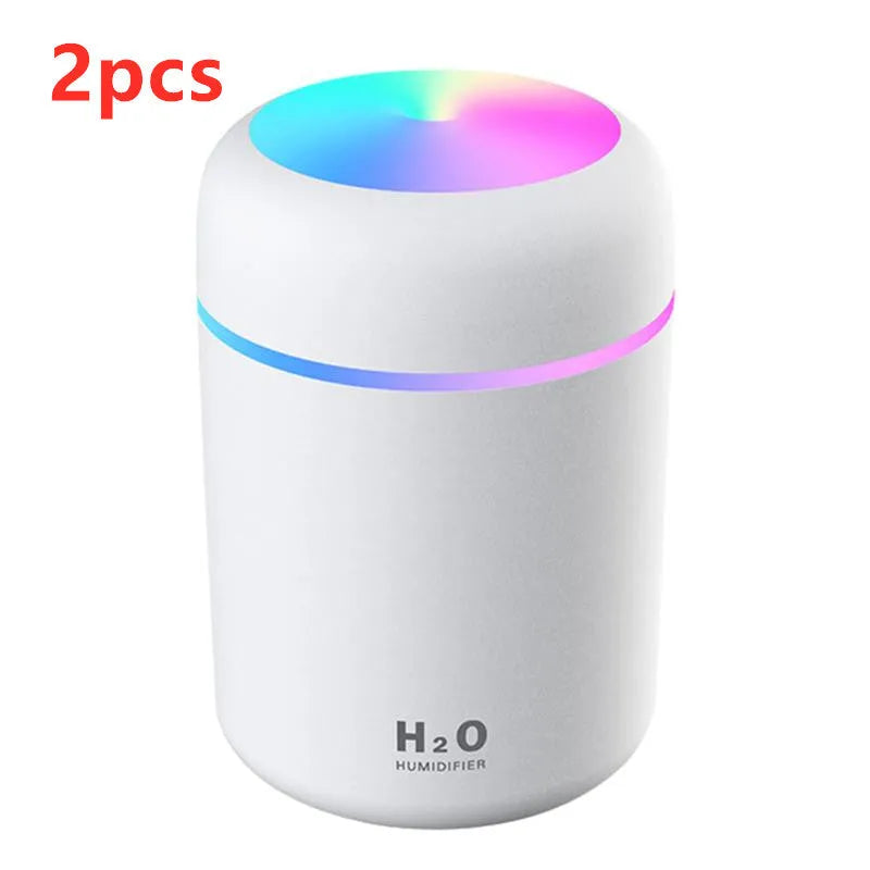 Pink USB mini humidifier with LED lights on wooden desk beside laptop