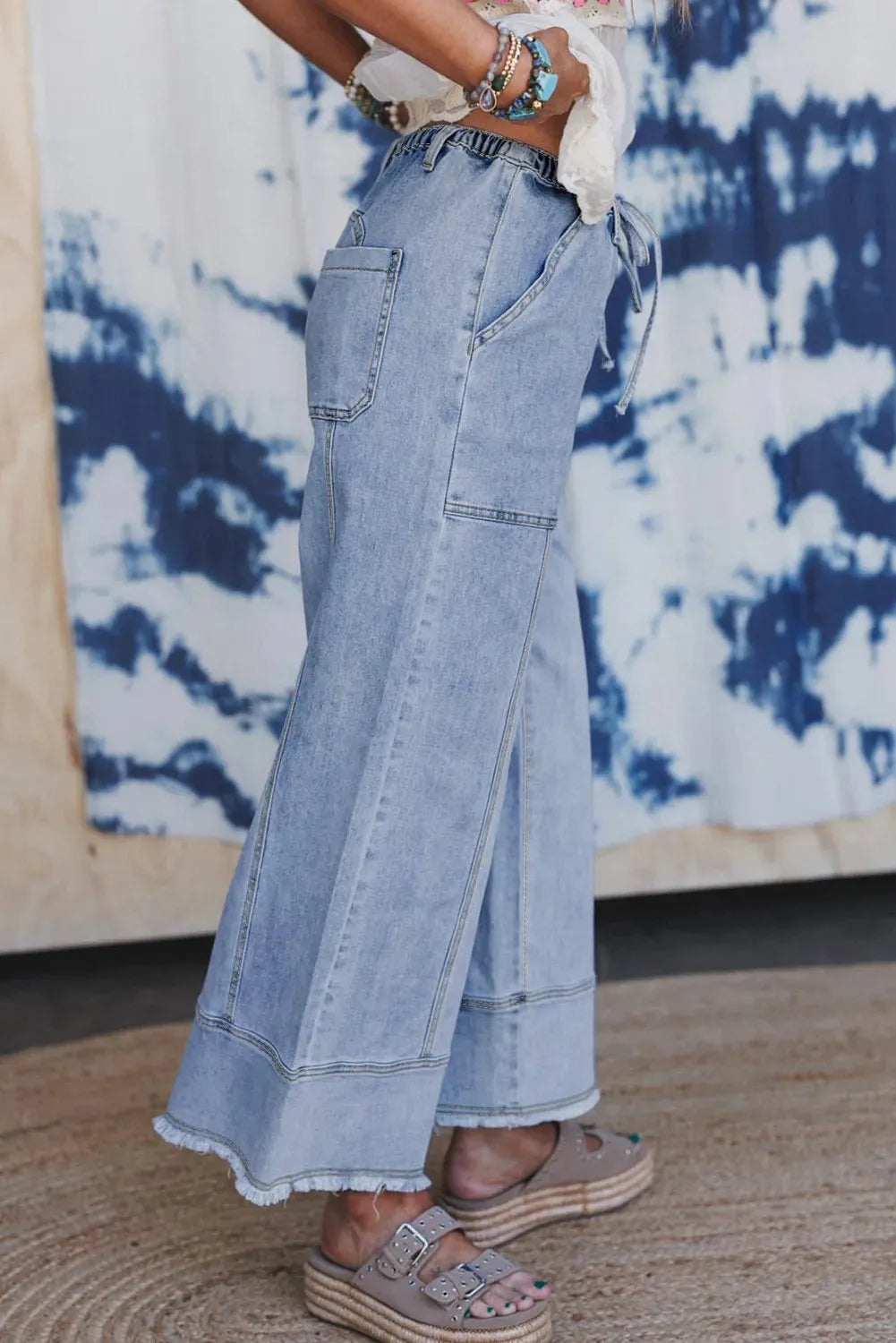 Women's beau blue wide-leg denim trousers on a hanger, showing drawstring waist and raw hem detail.