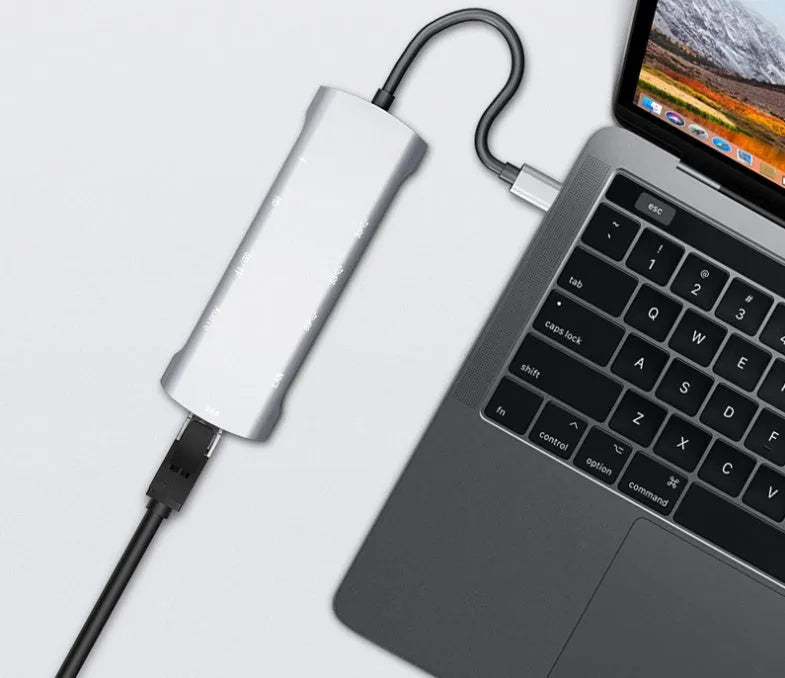 Grey aluminium USBC docking station with HDMI, VGA, USB ports and a short attached cable on a wooden desk