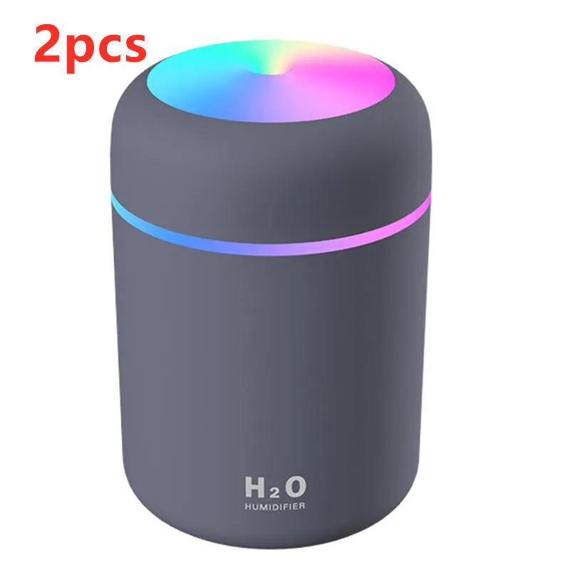 Pink USB mini humidifier with LED lights on wooden desk beside laptop