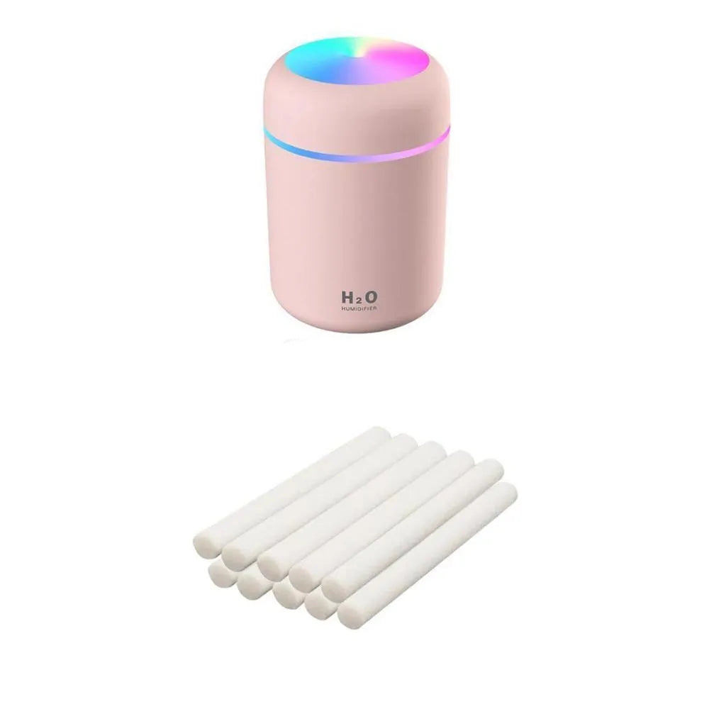 Pink USB mini humidifier with LED lights on wooden desk beside laptop