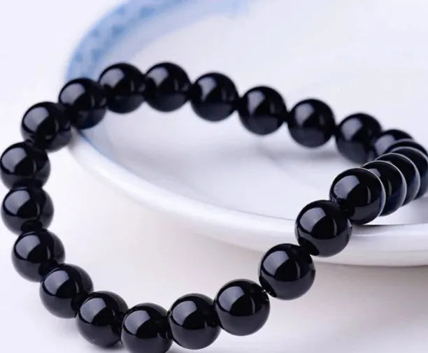 Close-up of a women's black agate bracelet with 8mm geometric beads on a black elastic cord.