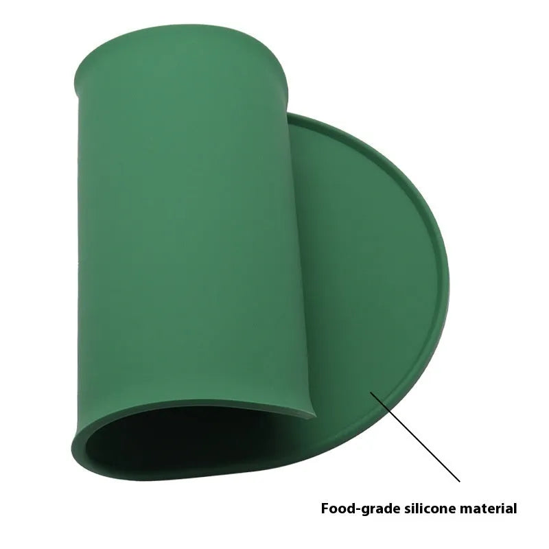 Green silicone cat feeding mat with raised edge containing a food bowl and scattered kibble on a kitchen floor.