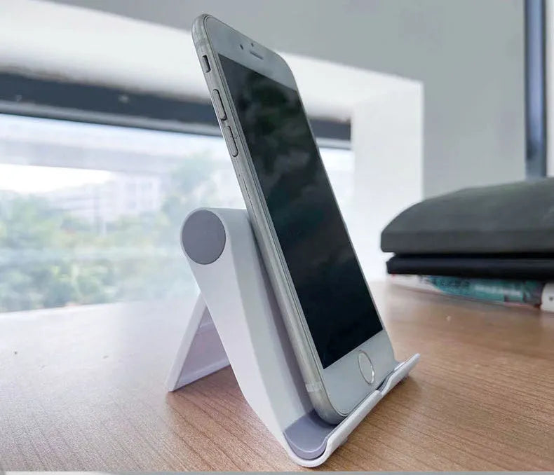 Black folding mobile phone stand holding a smartphone on a desk.