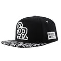 White and black adjustable cotton baseball cap with embroidered letters on the front, showing dome crown and adjustable strap.