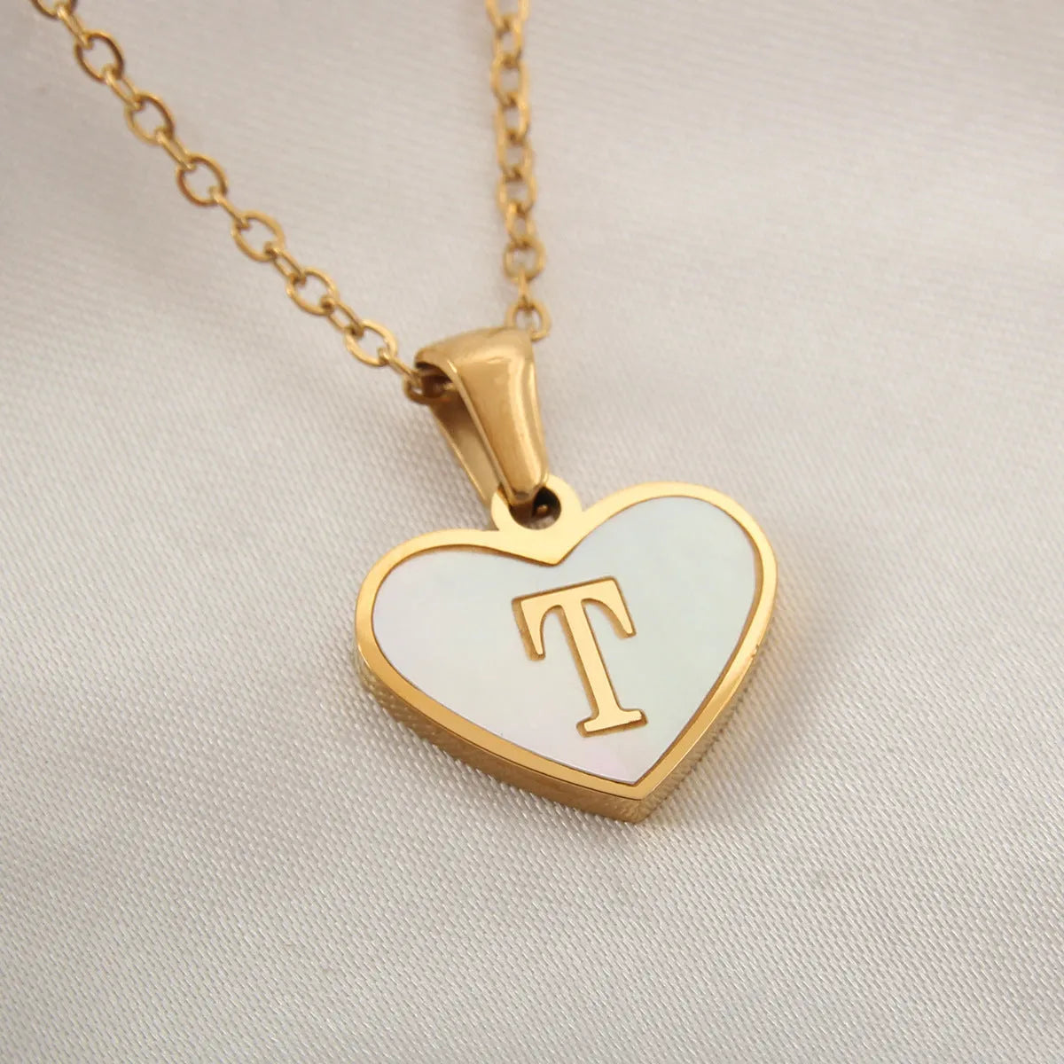 Gold-plated heart necklace with white shell pendant showing initial engraving on stainless steel chain