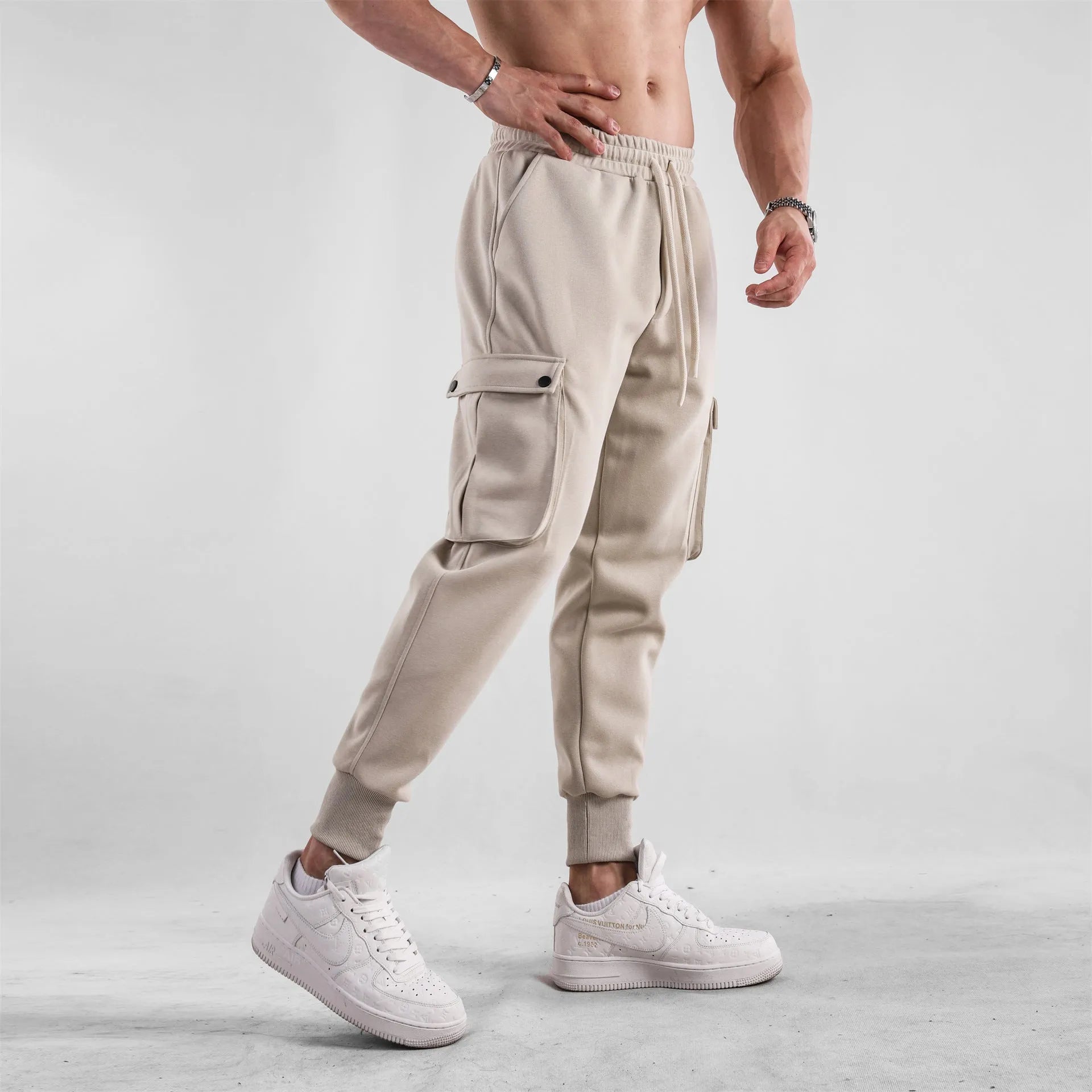 Men's beige ankle-tie loose-fit casual cotton trousers with side pockets on a neutral background.