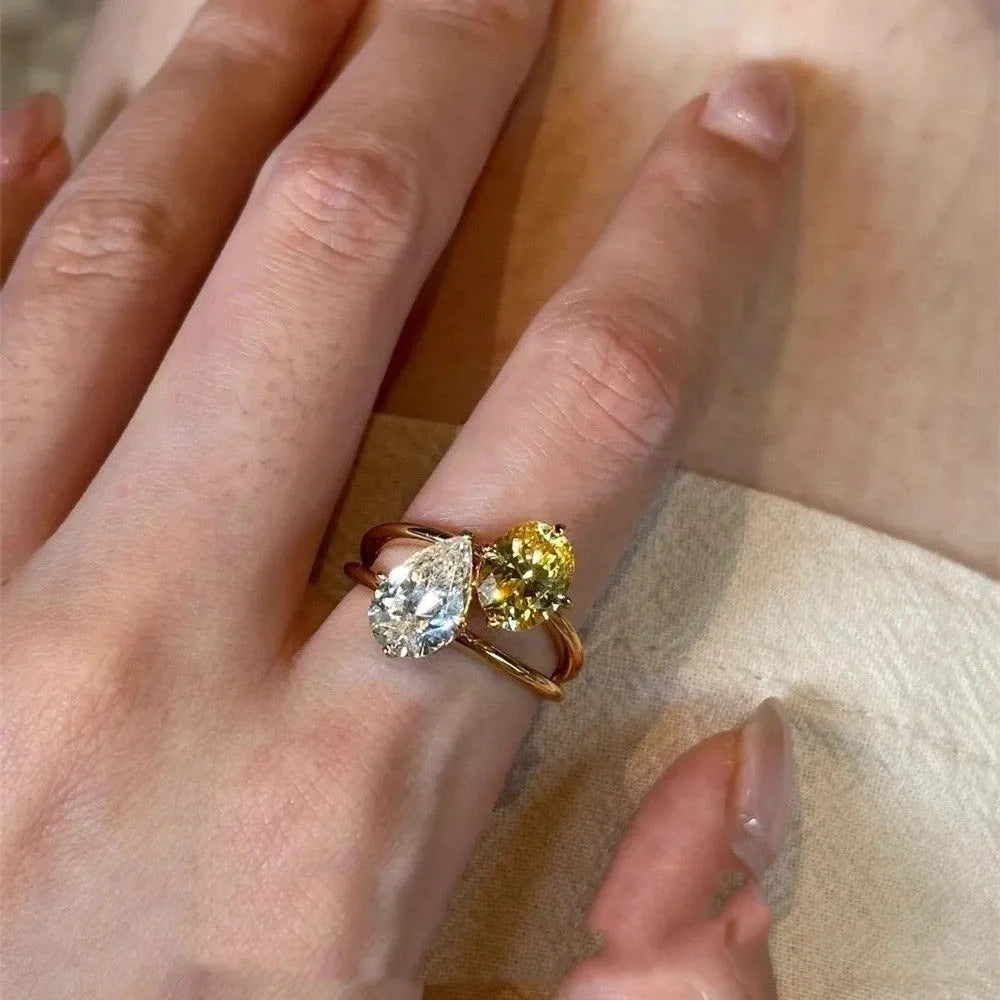 Copper geometric open ring with double zircon stones in a water drop design on a person's finger.