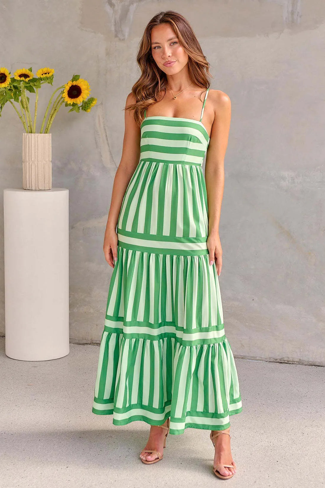 Woman wearing a striped backless suspender long dress with a square neck and side pockets.