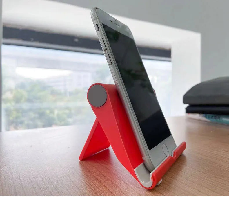 Black folding mobile phone stand holding a smartphone on a desk.