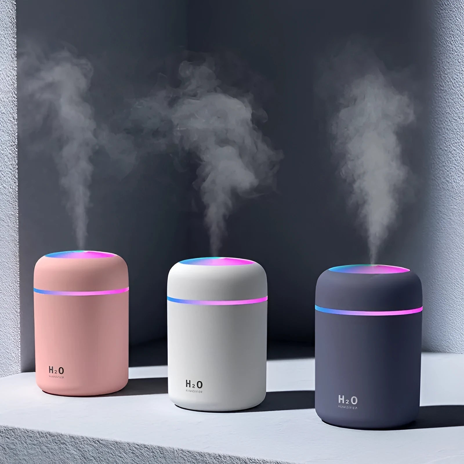 Pink USB mini humidifier with LED lights on wooden desk beside laptop