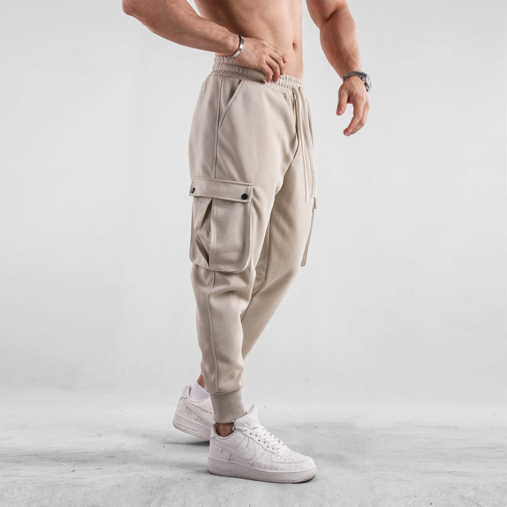 Men's beige ankle-tie loose-fit casual cotton trousers with side pockets on a neutral background.