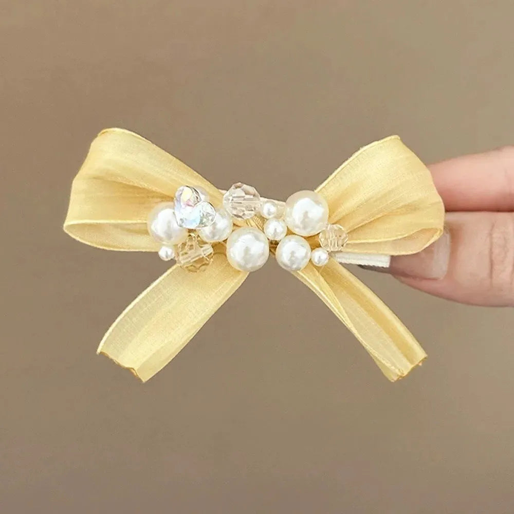 Yellow bow hair barrette with rhinestone and pearl details on duckbill clip
