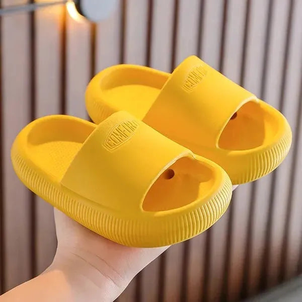 A pair of bright blue, one-piece EVA children's slippers with a textured non-slip sole, shown on a wooden floor.