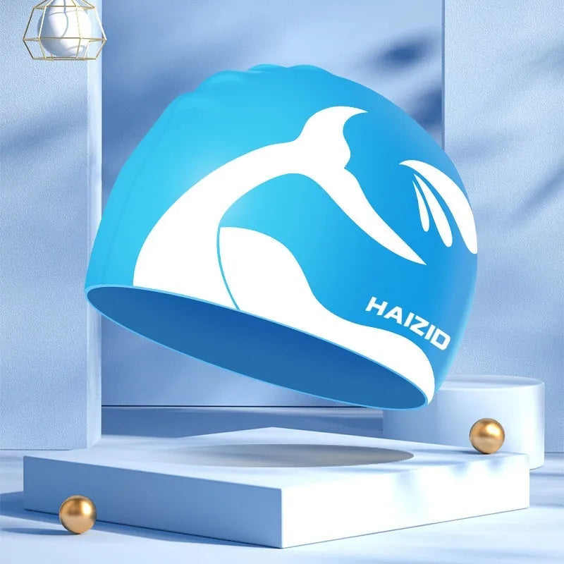 Silicone swimming cap with whale tail pattern and built-in ear protectors in black, blue, pink, and grey colours.