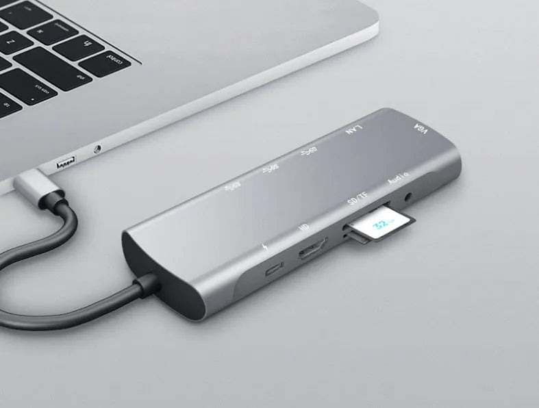 Grey aluminium USBC docking station with HDMI, VGA, USB ports and a short attached cable on a wooden desk