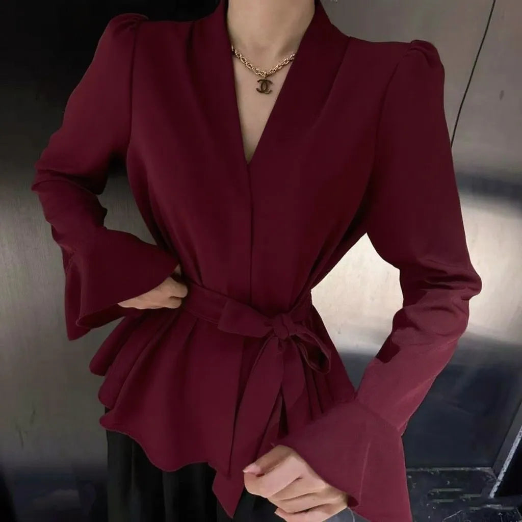 Woman wearing a black French-style shirt with an irregular collar, long bell sleeves, and a tie-front closure.