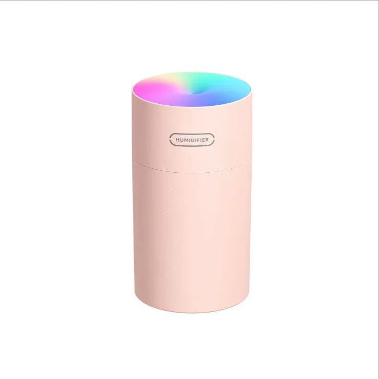 Pink USB mini humidifier with LED lights on wooden desk beside laptop
