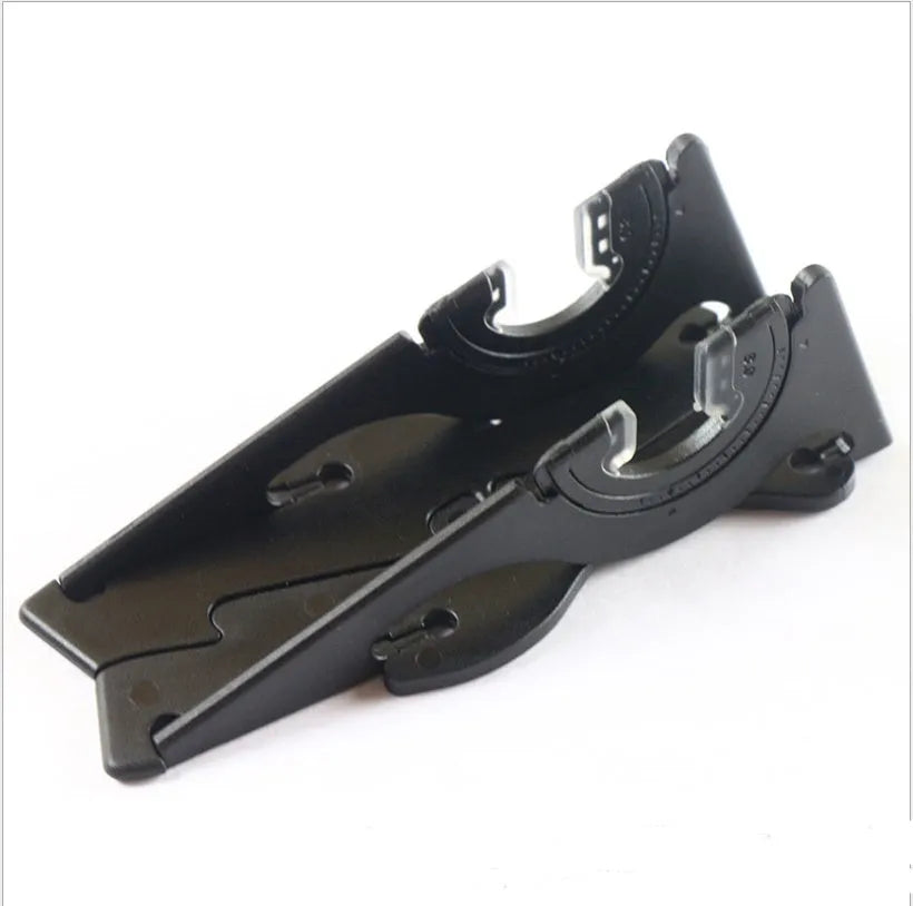 A flat, card-shaped black plastic mobile phone holder with its bracket unfolded, holding a smartphone on a wooden desk.