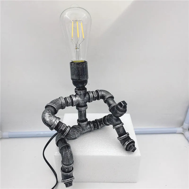 Industrial retro style iron pipe table lamp with water pipe robot design on a desk.