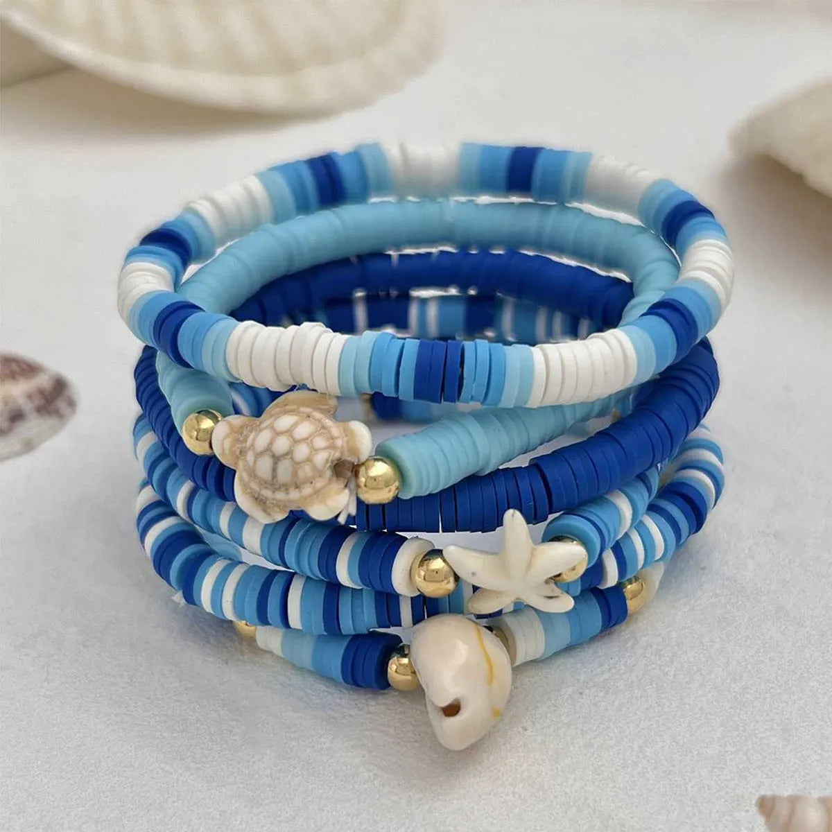 Six handmade Bohemian blue polymer clay bracelets with shell designs and geometric shapes arranged together