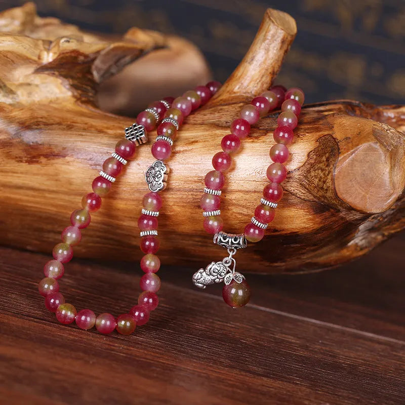 A handmade bracelet with geometrically cut watermelon crystal beads and a red Chinese knot closure on a white background.