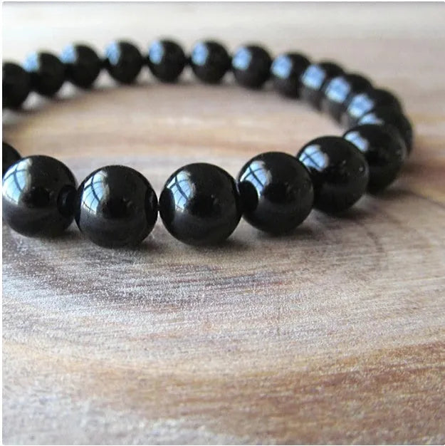 Close-up of a women's black agate bracelet with 8mm geometric beads on a black elastic cord.