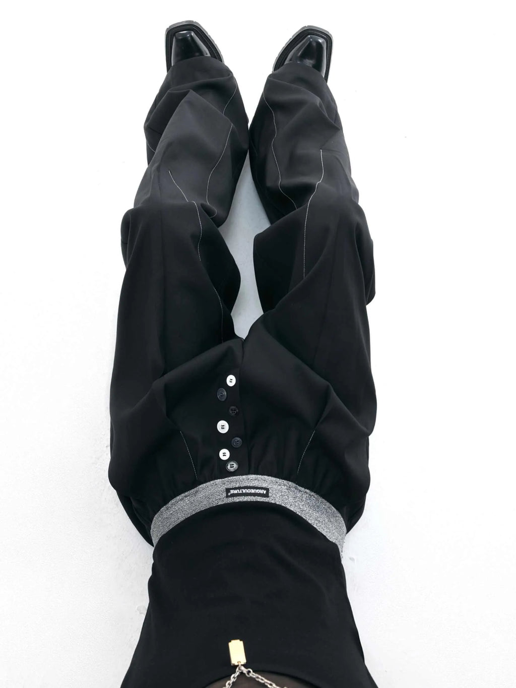 Straight-leg high-waisted trousers in black with a drooping waistband and button detail on a neutral background.