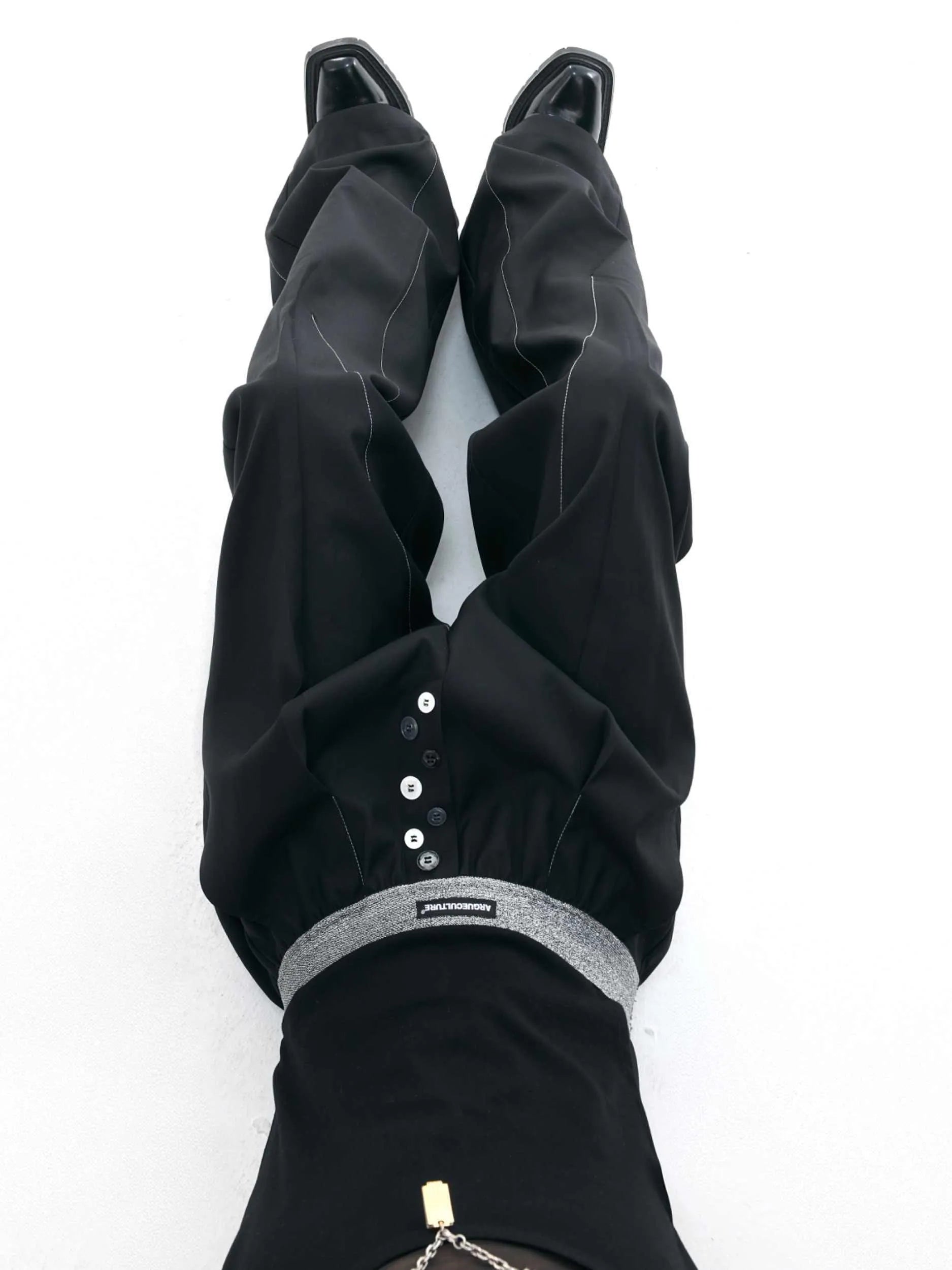 Straight-leg high-waisted trousers in black with a drooping waistband and button detail on a neutral background.