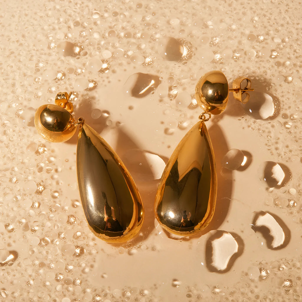 A pair of gold geometric hemisphere earrings with a water droplet pendant design on a white background.