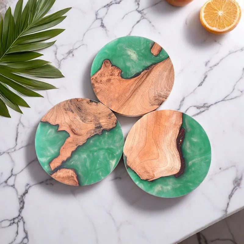 Round and square black and green resin coasters with wood texture for tea pots on a table.