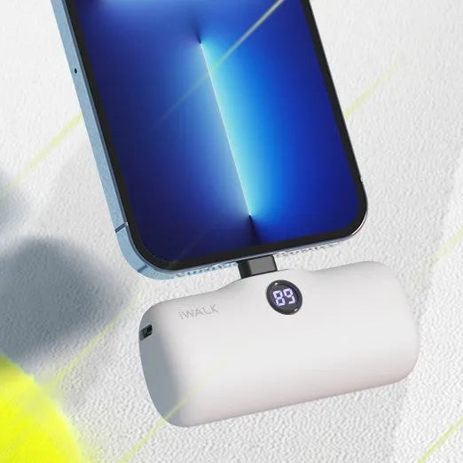 Small white lipstick-shaped power bank showing digital battery percentage display on a wooden table.