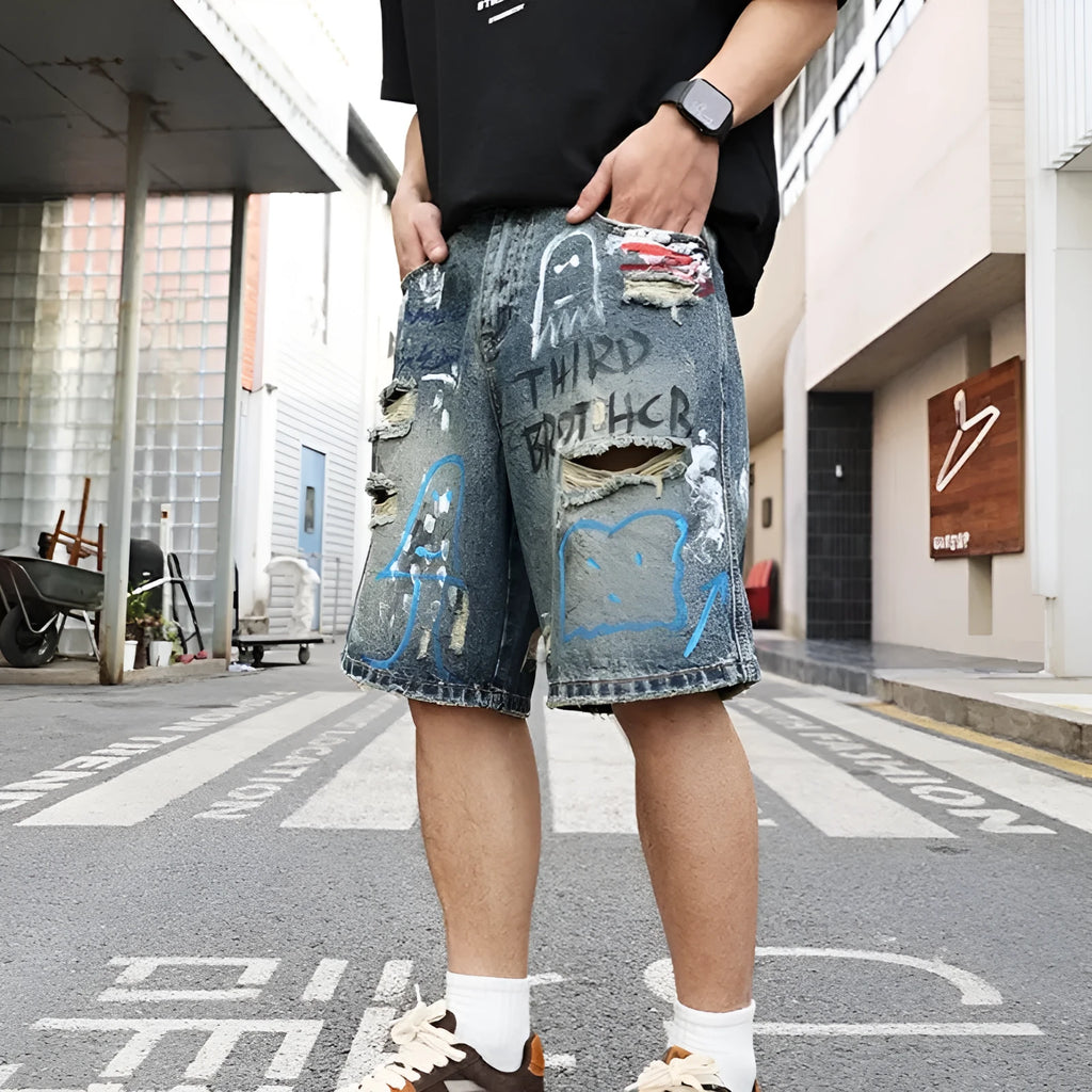 Blue denim shorts for men with ripped knees and graffiti design, featuring a straight leg and zipper fly.