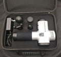 Black ABS fascia massage gun with four different coloured attachment heads on a grey surface.