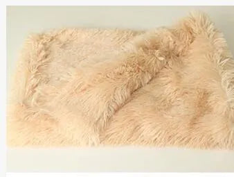 Soft grey long plush pet blanket for dogs on a wooden floor next to a kennel.