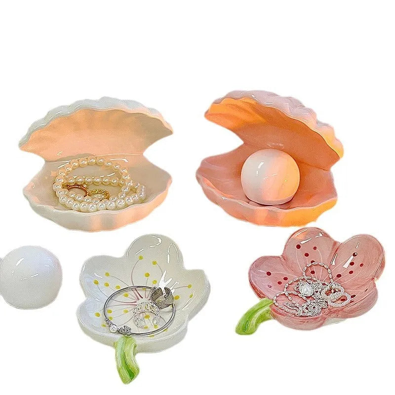 White porcelain scallop shell tray with optional warm LED night light, holding small jewellery on a bedside table.
