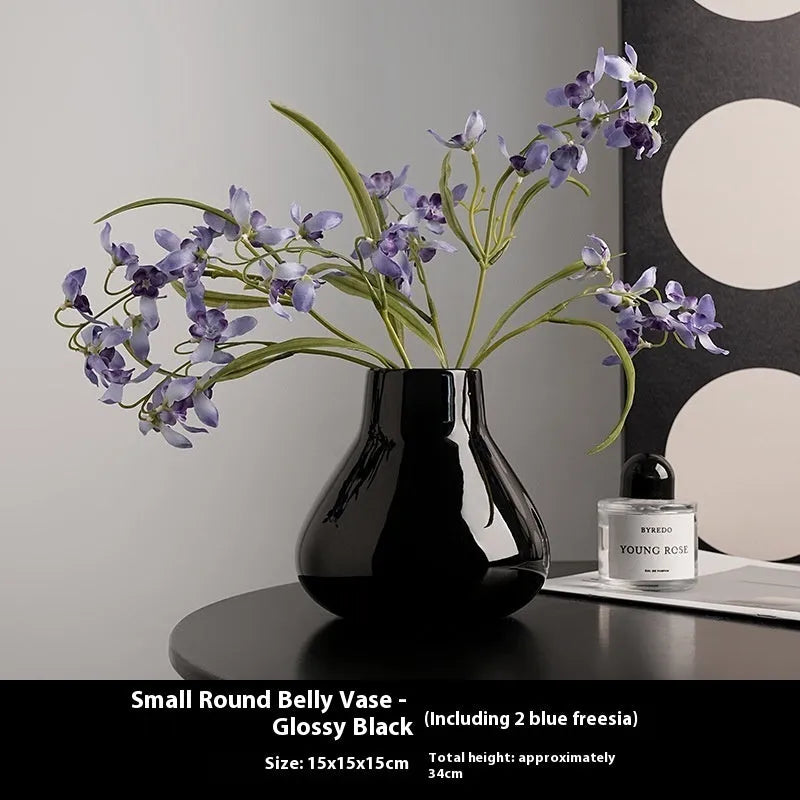 Modern round belly ceramic vase with coloured glaze, shown in black and white, some with artificial flowers.