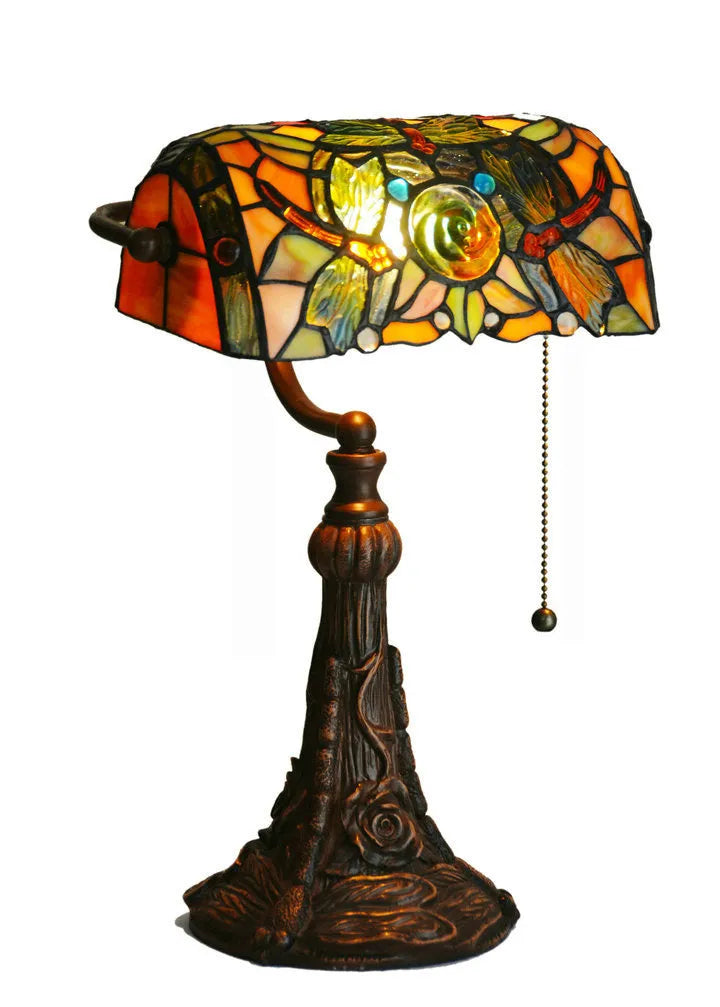 Tiffany style table lamp with colourful stained glass shade and resin base on a wooden table.