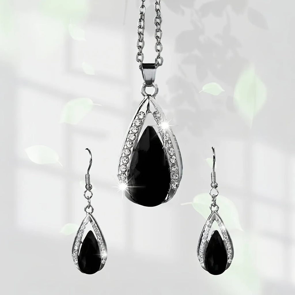 Close-up of a black alloy teardrop pendant necklace and matching drop earrings with glass details on a plain background.